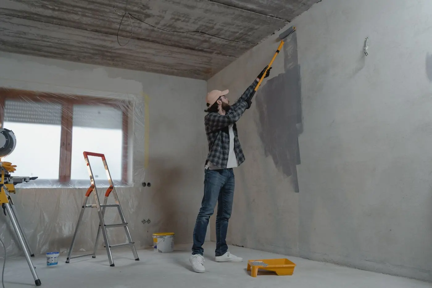 Man werkt met een roller op een lange steel aan een grijze muur in een kale ruimte